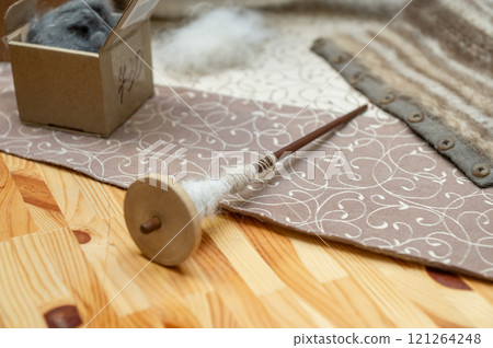 Handcrafted wooden drop spindle with wool on patterned fabric surface Handcrafted wooden drop spindle with wool on patterned fabric surface 121264248