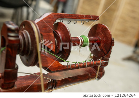 Distaff Day Vintage wooden spinning wheel with green thread close-up Distaff Day Vintage wooden spinning wheel with green thread close-up 121264264