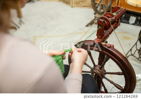 Distaff Day Caucasian female adult spinning yarn on traditional wheel in workshop 121264269