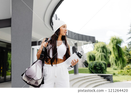 Beautiful woman ready to start her training. Energetic woman is going to gym with sports bag and bottle in hand Beautiful woman ready to start her training. Energetic woman is going to gym with sports bag and bottle in hand 121264420