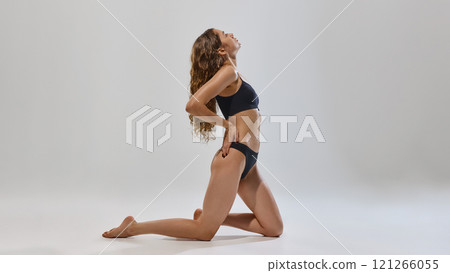 Confident, young, slender woman posing in black underwear and showing her fit, slim body against grey studio background. Confident, young, slender woman posing in black underwear and showing her fit, slim body against grey studio background. 121266055