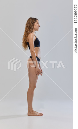 Side view photo of young attractive lady with slim figure posing in lingerie against grey studio background. Side view photo of young attractive lady with slim figure posing in lingerie against grey studio background. 121266072
