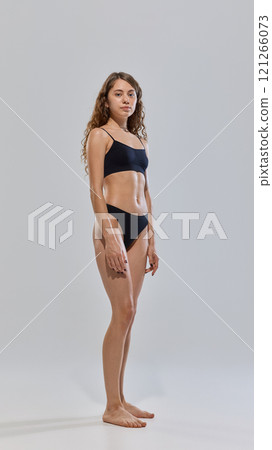 Young attractive woman posing in black lingerie showing her slim figure against grey studio background. Fitness. Young attractive woman posing in black lingerie showing her slim figure against grey studio background. Fitness. 121266073