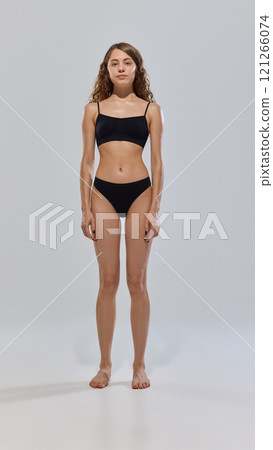 Young attractive woman posing in black lingerie showing her slim figure against grey studio background. Fitness. Young attractive woman posing in black lingerie showing her slim figure against grey studio background. Fitness. 121266074