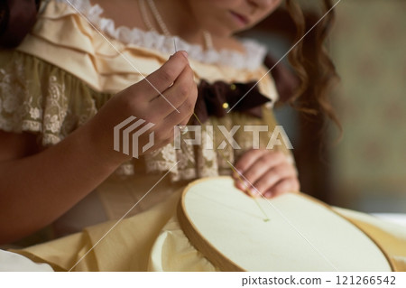 Side view detail shot of young lady guiding thread through fabric doing intricate embroidery in vintage setting, copy space 121266542