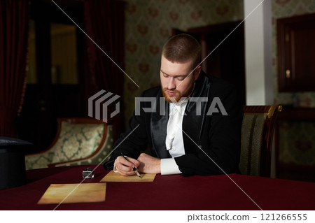 Portrait of young gentleman writing letters with ink while sitting at table in classic interior lit by soft natural light, copy space 121266555
