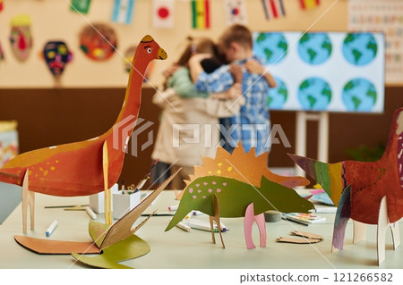 Close up background image of colorful handmade dinosaur figures painted during art and craft class with group of kids hugging in background copy space 121266582