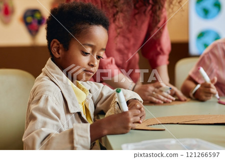Portrait of young African American boy painting handmade dinosaur figure made of cardboard while enjoying art and craft class in school copy space Portrait of young African American boy painting handmade dinosaur figure made of cardboard while enjoying art and craft class in school copy space 121266597