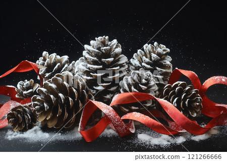 Christmas composition with snow falling on pine cones and red ribbons on a black background 121266666