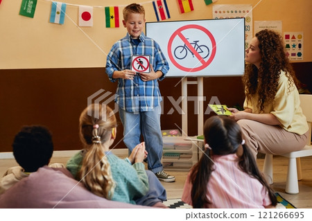 Full length shot of smiling young boy holding No walking sign while presenting road safety rules to kids in school classroom copy space 121266695