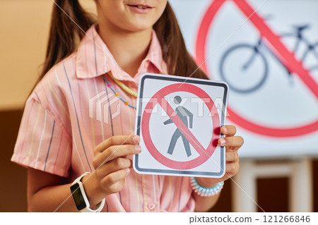 Close up of young girl holding No bicycles sign while learning road safety rules for children in primary school classroom copy space 121266846