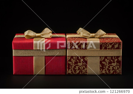 Two red christmas gift boxes with gold ribbons are lying on a black background, suggesting luxury and celebration 121266970