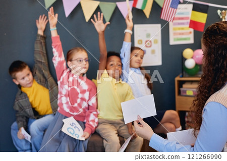 Close up of female teacher showing card to multiethnic group of children raising hands in blurred background copy space Close up of female teacher showing card to multiethnic group of children raising hands in blurred background copy space 121266990