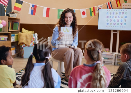 Portrait of smiling female teacher showing alphabet cards to children while teaching English in primary school classroom 121266994
