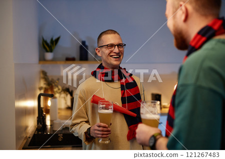 Waist up portrait of smiling sports fan talking to friend during after game party in home kitchen 121267483