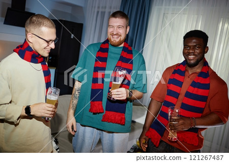 Front view portrait of three smiling sports fans in team colored scarves partying and holding drinks while enjoying victory celebration, shot with flash 121267487