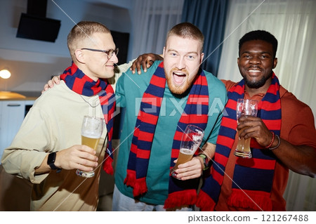 Waist up portrait of three cheerful sports fans wearing matching team scarves and holding beer glasses while cheering together during after game party, shot with flash Waist up portrait of three cheerful sports fans wearing matching team scarves and holding beer glasses while cheering together during after game party, shot with flash 121267488