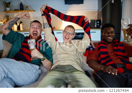 Front view portrait of three adult men watching sports match on TV and cheering with accessories in team colors, copy space 121267494