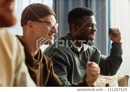 Side view portrait of excited sports fans cheering in victory while sitting on couch at home and watching game Side view portrait of excited sports fans cheering in victory while sitting on couch at home and watching game 121267529
