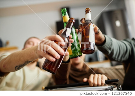 Close up of beer bottles raised in toast with sports fans cheering while watching game at home, copy space 121267540