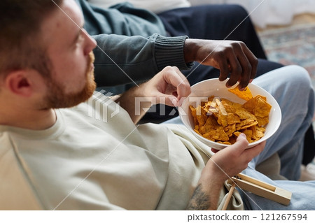 High angle closeup of man holding bowl with chips and snacks while watching TV with friends at home, copy space 121267594