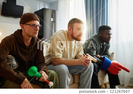 Multiethnic group of focused young men watching game on TV intently while sitting on couch at home in sunlight, copy space Multiethnic group of focused young men watching game on TV intently while sitting on couch at home in sunlight, copy space 121267607