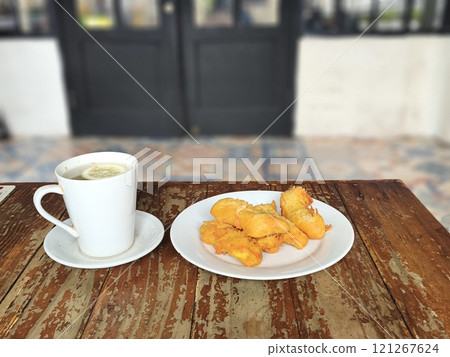 A plate of golden brown banana fritters sits beside a cup of hot lemon. A plate of golden brown banana fritters sits beside a cup of hot lemon. 121267624