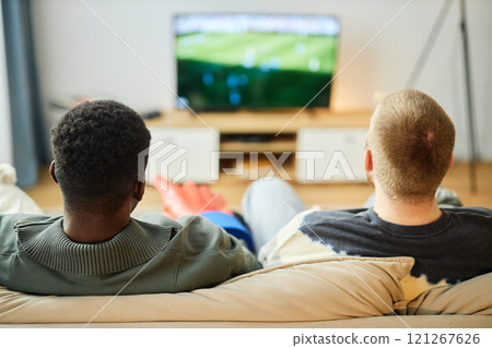 Back view of two adult men watching football match on TV at home sitting on couch, copy space Back view of two adult men watching football match on TV at home sitting on couch, copy space 121267626