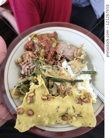 A person is skillfully holding a plate filled with rice and assorted vegetables 121267658