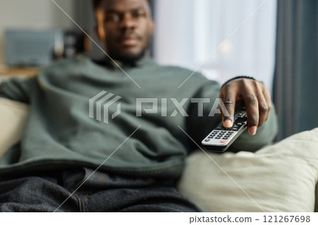 Close up of African American man watching TV at home with focus on hand holding remote, copy space 121267698