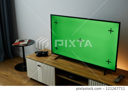 At angle background image of big TV with green screen mock up on modern Tv stand in home setting, copy space 121267711