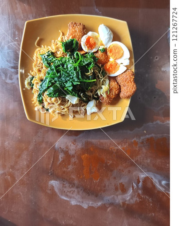 A plate of instant noodles topped with spinach, hard-boiled eggs, and fried fish cakes. A plate of instant noodles topped with spinach, hard-boiled eggs, and fried fish cakes. 121267724