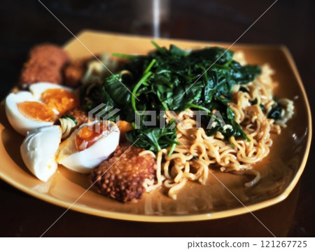A plate of instant noodles topped with spinach, hard-boiled eggs, and fried fish cakes. A plate of instant noodles topped with spinach, hard-boiled eggs, and fried fish cakes. 121267725