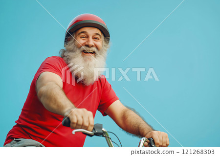 Happy smiling senior man with white beard riding bicycle wearing helmet on blue background 121268303