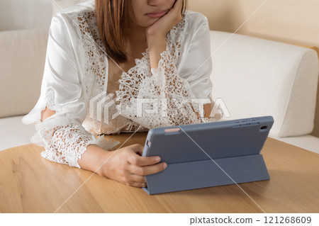 Woman in white silk sleepwear reads tablet at night. 121268609
