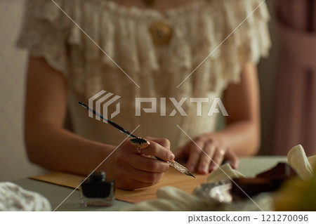 Close up of classic young lady writing letter with focus on female hands holding intricate ink pen and ornate ring, copy space Close up of classic young lady writing letter with focus on female hands holding intricate ink pen and ornate ring, copy space 121270096