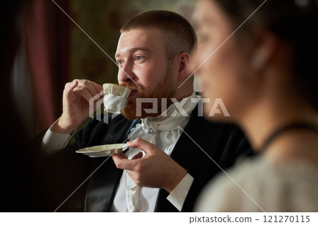 Side view portrait of young gentleman sipping tea delicately from porcelain teacup in classic setting 121270115