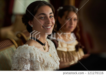 Portrait of young woman in lace gown smiling at companion in classic dining setting, copy space Portrait of young woman in lace gown smiling at companion in classic dining setting, copy space 121270116