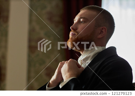 Side view portrait of classic young gentleman adjusting white cravat while looking in mirror preparing for ball in classical interior with natural light, copy space Side view portrait of classic young gentleman adjusting white cravat while looking in mirror preparing for ball in classical interior with natural light, copy space 121270123