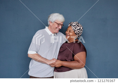 Minimal studio portrait of affectionate senior couple with Caucasian man and Black woman embracing gently and smiling against blue background Minimal studio portrait of affectionate senior couple with Caucasian man and Black woman embracing gently and smiling against blue background 121270167