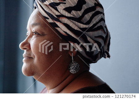 Minimal closeup portrait of Black senior woman wearing headscarf and smiling looking away in soft natural light accentuating profile 121270174
