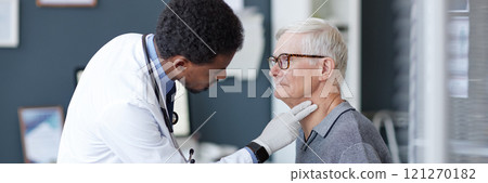 Cropped image of African American doctor wearing gloves carefully palpating neck of senior patient during examination in clinic, copy space 121270182