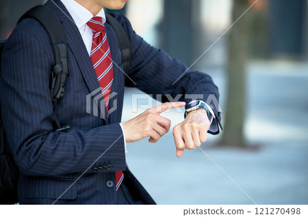 A businessman in a suit looking at a smartwatch 121270498
