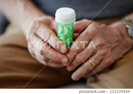 Close up of elderly man holding green prescription pill bottle in hands suffering from chronic illness, copy space 121270544