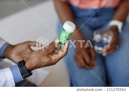 Close up of unrecognizable African American doctor holding green pill bottle while explaining medication side effects to patient during consultation in clinic, copy space Close up of unrecognizable African American doctor holding green pill bottle while explaining medication side effects to patient during consultation in clinic, copy space 121270562
