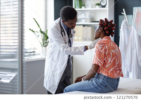 Waist up portrait of doctor wearing lab coat examining young woman by palpating neck and lymph nodes during consultation in clinic 121270570