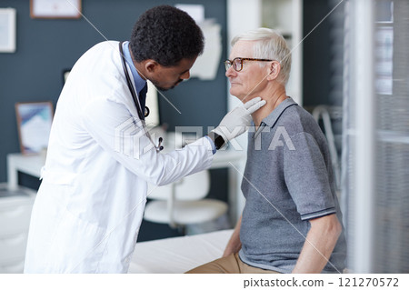Side view scene of African American doctor wearing gloves carefully palpating neck of senior patient during examination in clinic, copy space 121270572