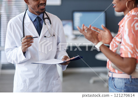 Cropped shot of African American doctor wearing lab coat and holding clipboard while talking to female patient in clinic, copy space Cropped shot of African American doctor wearing lab coat and holding clipboard while talking to female patient in clinic, copy space 121270614