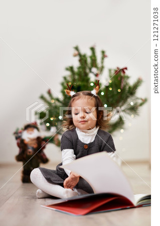 Cute little child girl reads a book near the Christmas tree at home 121271038