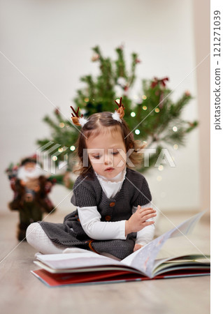 Cute little child girl reads a book near the Christmas tree at home 121271039